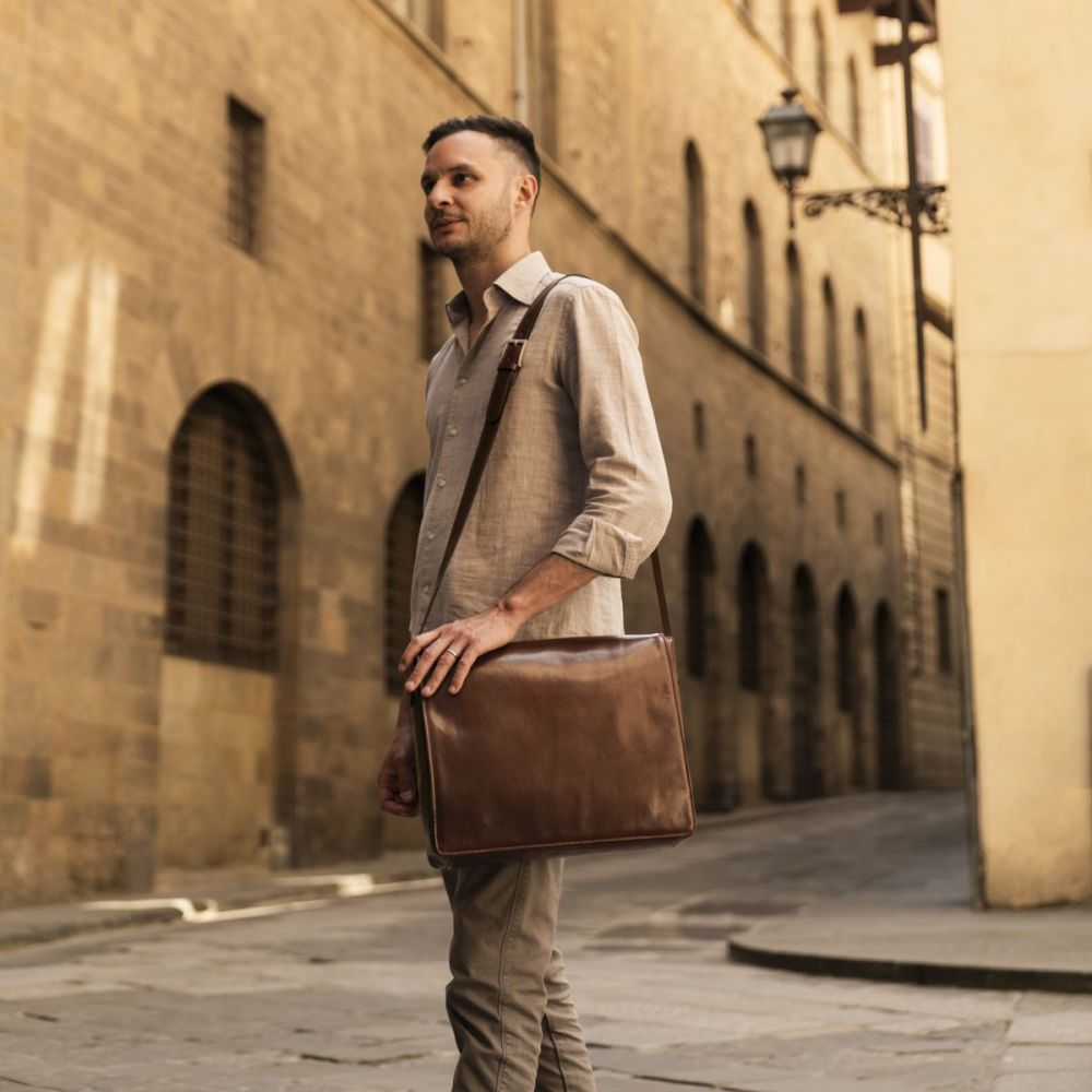 Uomo con borsa messenger in pelle marrone in una piazza