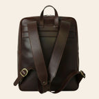 Zaino in pelle marrone scuro con fascia trolley, maniglia e zip frontale.