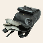 Zaino in pelle nero aperto: interno chiaro, tasche e tracolla con fibbia