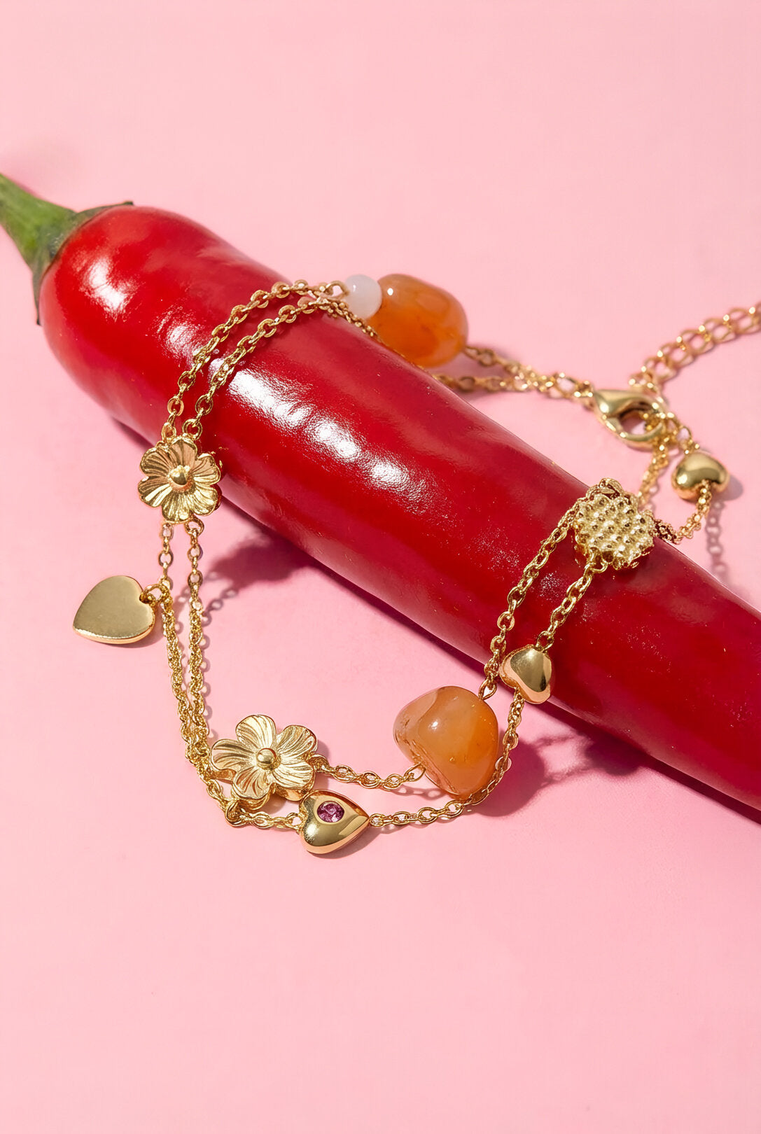 Bracciale con ciondoli arancioni tra fiori e cuori, posato su un peperoncino rosso.