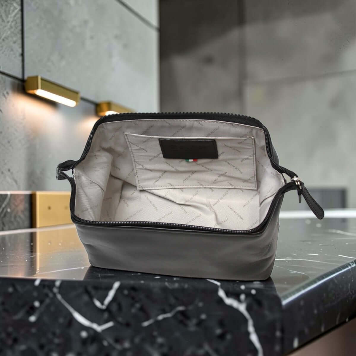 Porta cosmetici in pelle scura aperto: fodera chiara e tasca interna.