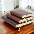 Diario in pelle marrone con tre formati impilati: SMALL, MEDIUM, LARGE, con segnalibro.