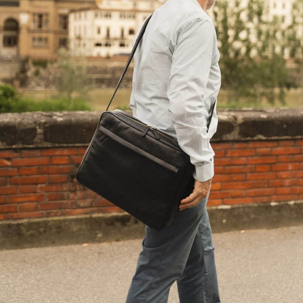 Uomo che indossa un messenger in vacchetta unisex mentre passeggia lungo un muro di mattoni.