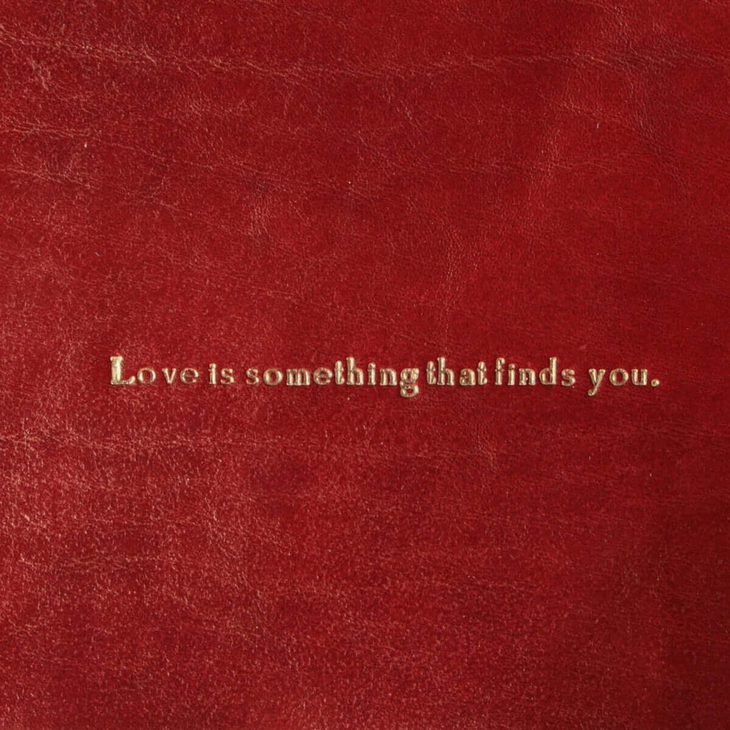 Vuotatasche in pelle rossa con scritta: Love is something that finds you.