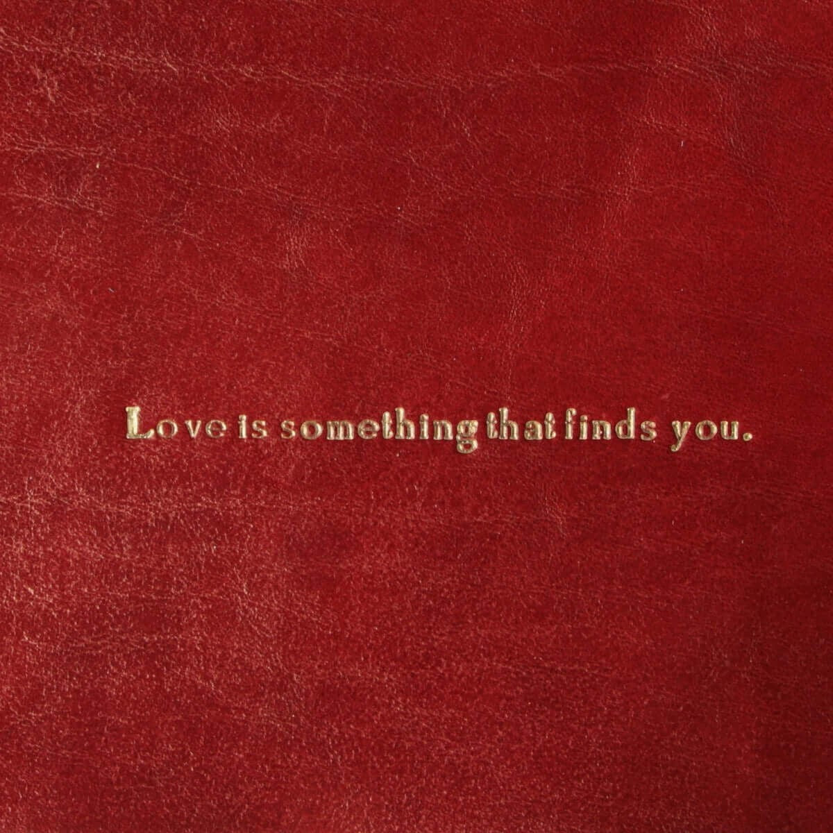 Vuotatasche in pelle rossa con scritta: Love is something that finds you.