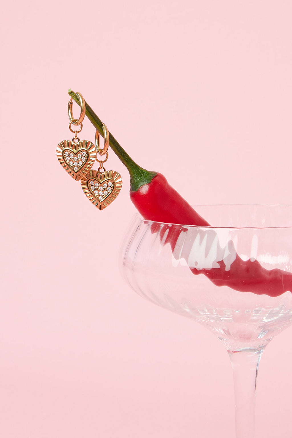 Orecchini cuori luminosi appesi a un bicchiere con peperoncino su sfondo rosa.