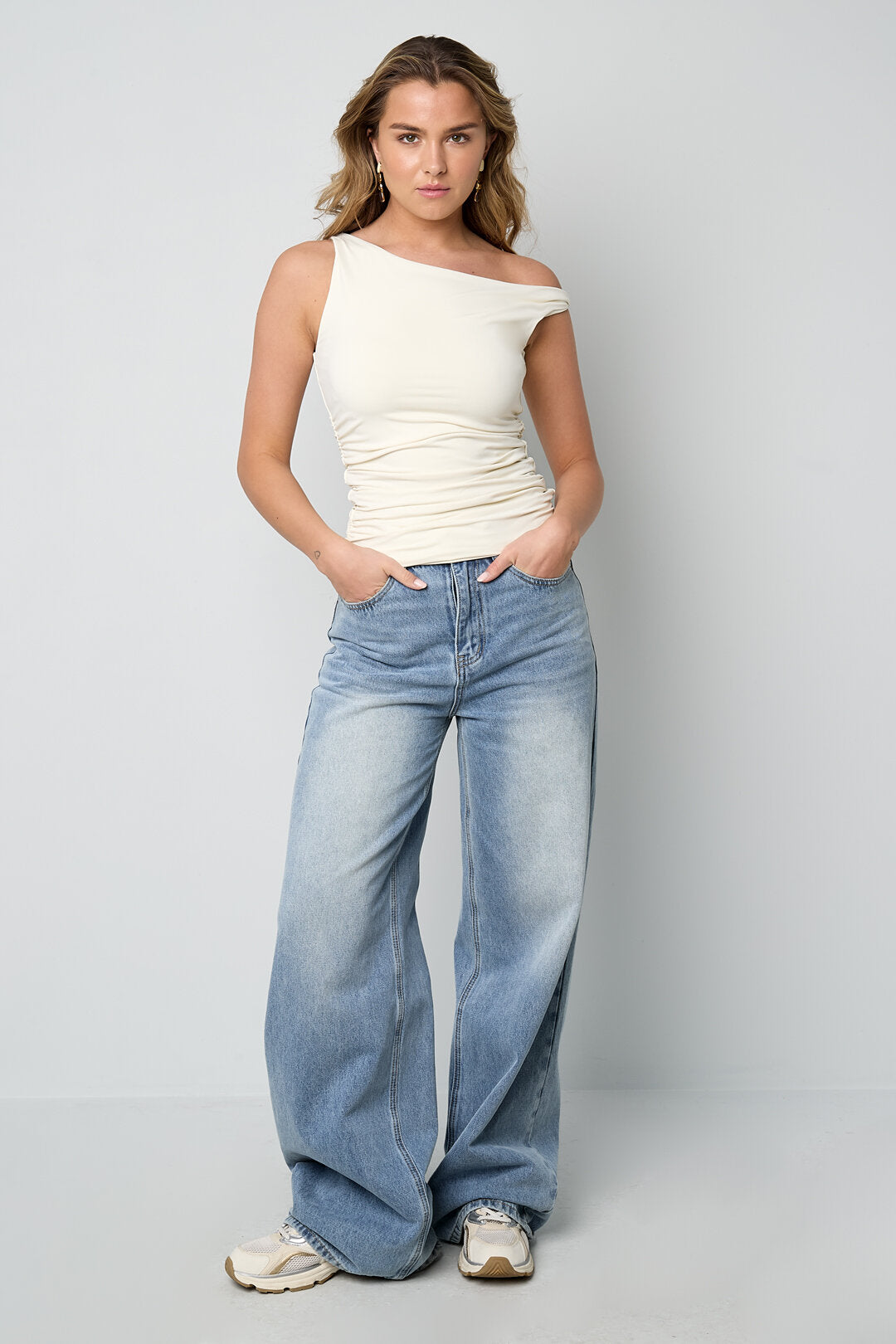 Modella che indossa una canotta basic uomo e jeans larghi, in posa su sfondo neutro.