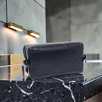 Porta cosmetici in pelle scura sagomato con zip e maniglia laterale.