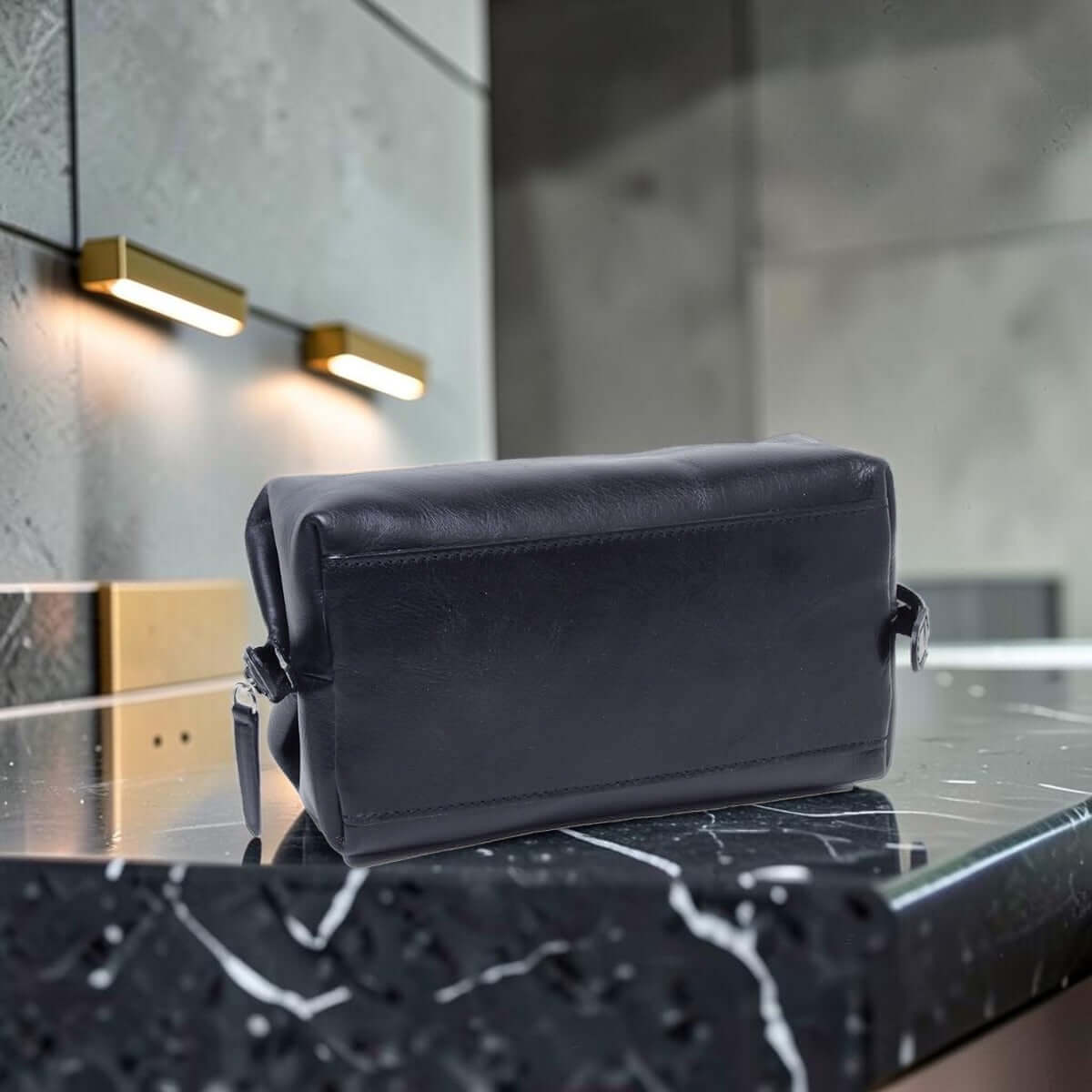 Porta cosmetici in pelle scura sagomato con zip e maniglia laterale.