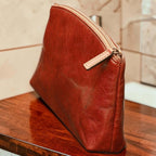 Astuccio cosmetici in pelle marrone con zip perimetrale e fibbia laterale.