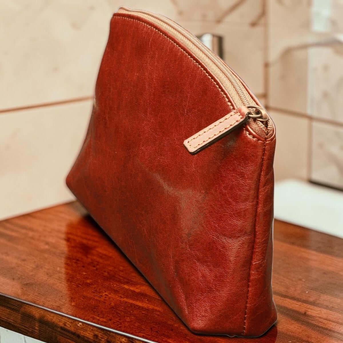 Astuccio cosmetici in pelle marrone con zip perimetrale e fibbia laterale.
