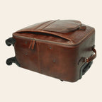 Trolley in pelle marrone con profilo rigido, patta superiore e manico laterale; ruote.