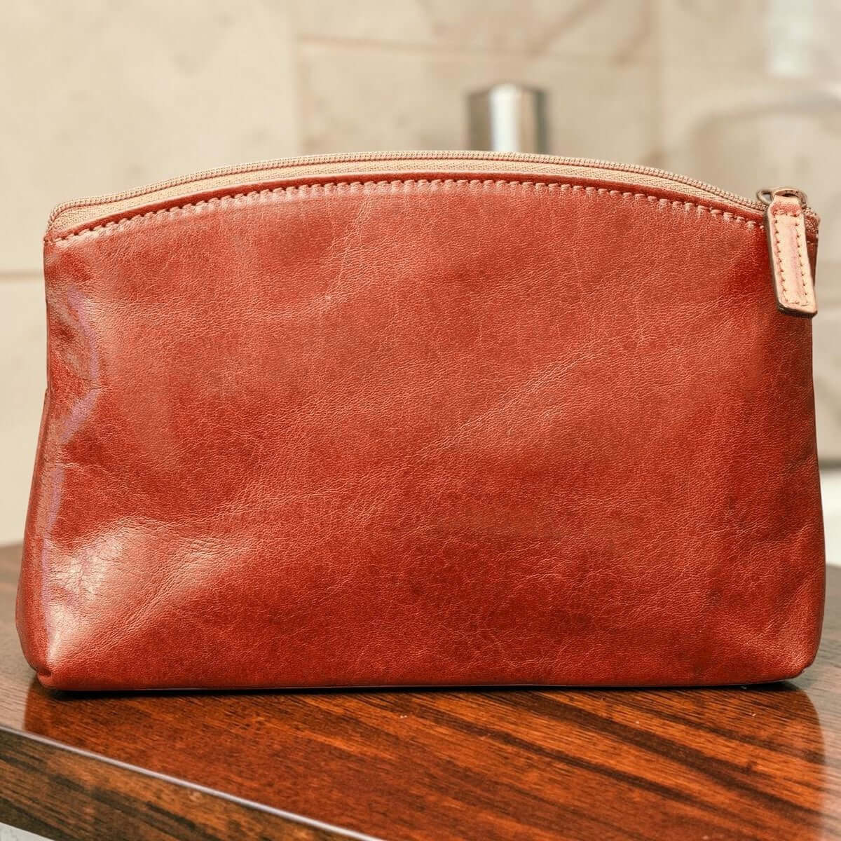 Astuccio cosmetici in pelle marrone, zip superiore e patta metallica.