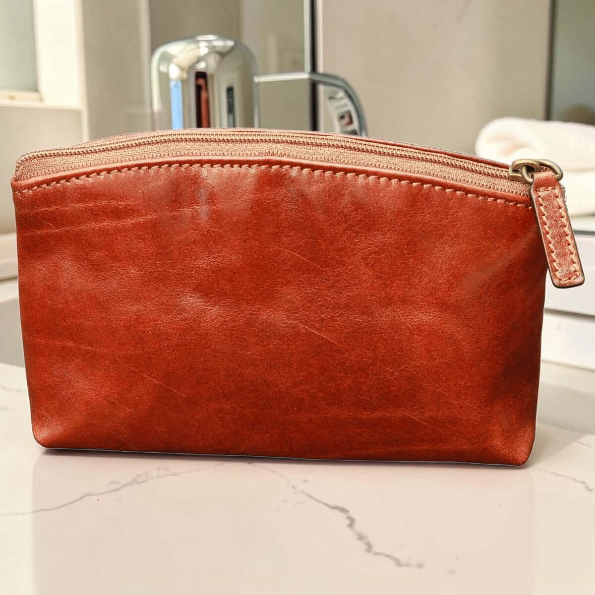 Beauty case in pelle marrone con zip, angoli arrotondati e gancio metallico