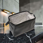 Porta cosmetici in pelle scura aperto con fodera chiara e passante laterale.