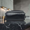 Porta cosmetici in pelle scura compatto con manici laterali e zip superiore.