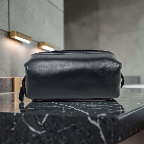 Porta cosmetici in pelle scura compatto con manici laterali e zip superiore.