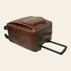 Trolley in pelle marrone con maniglia estesa e tracolla laterale; ruote.