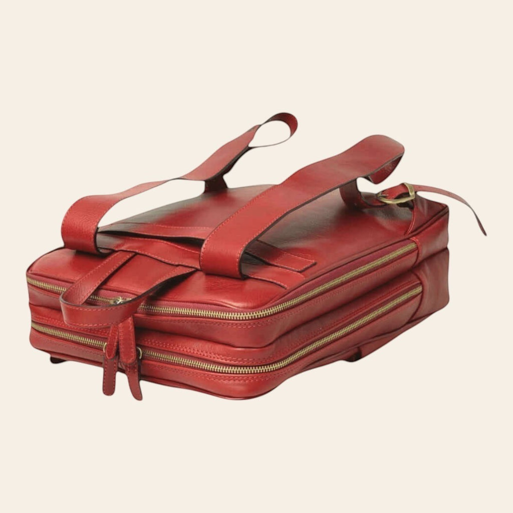 Mochila de piel de becerro en color rojo, colocada en horizontal con dos compartimentos con cremallera y tirantes visibles
