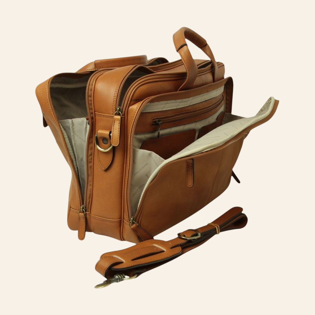 Borsa porta laptop in pelle color coloniale; vista laterale a tre quarti aperta con più scomparti con zip, fodera chiara e tracolla staccabile